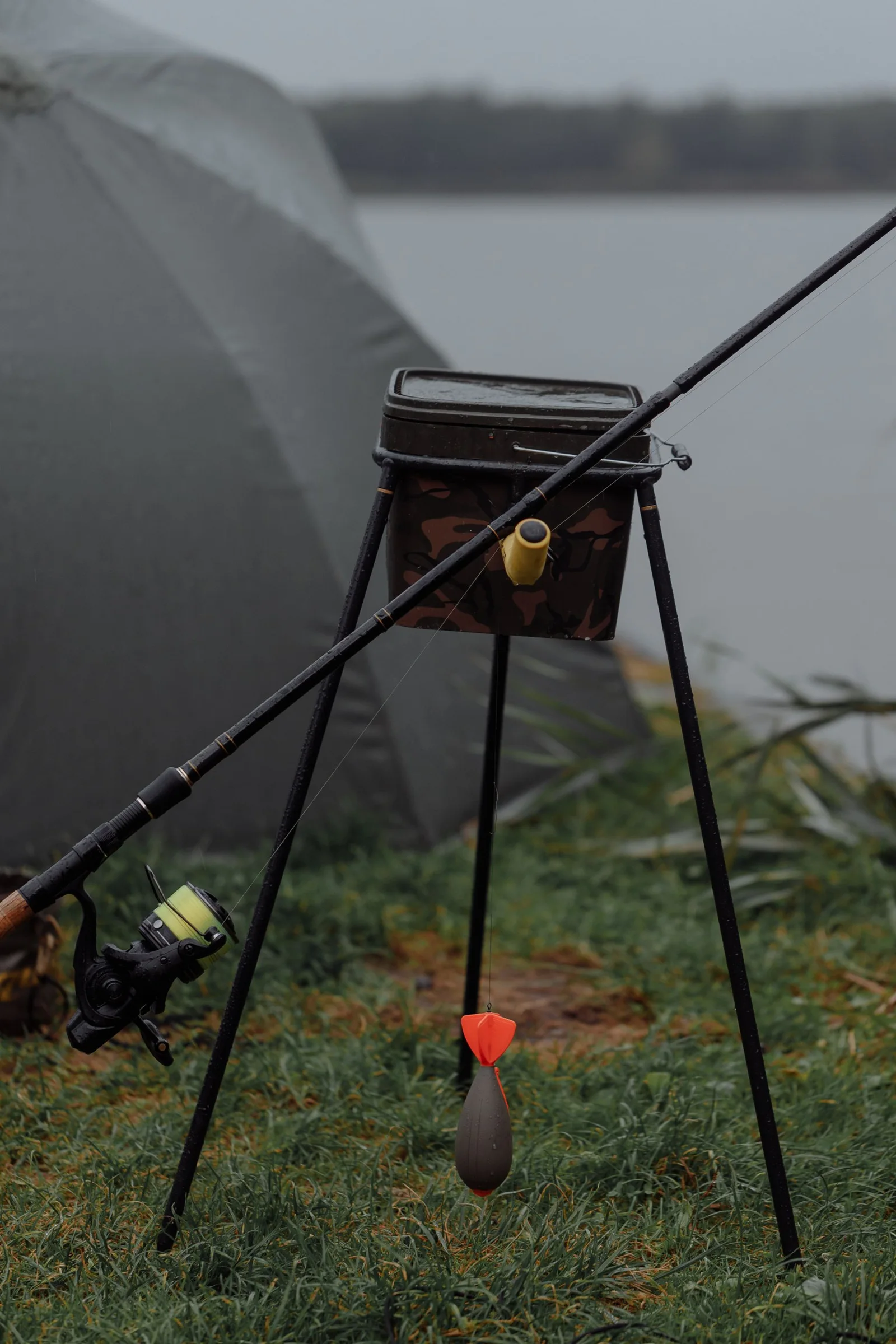 A fishing rod and reel resting on grass beside water.