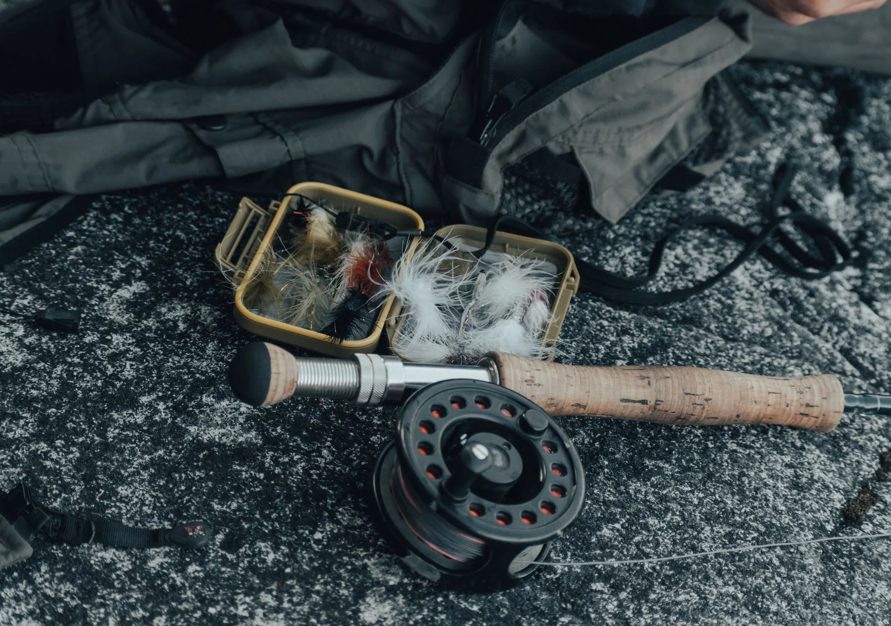 Fly fishing rod and reel beside a box of colorful flies.
