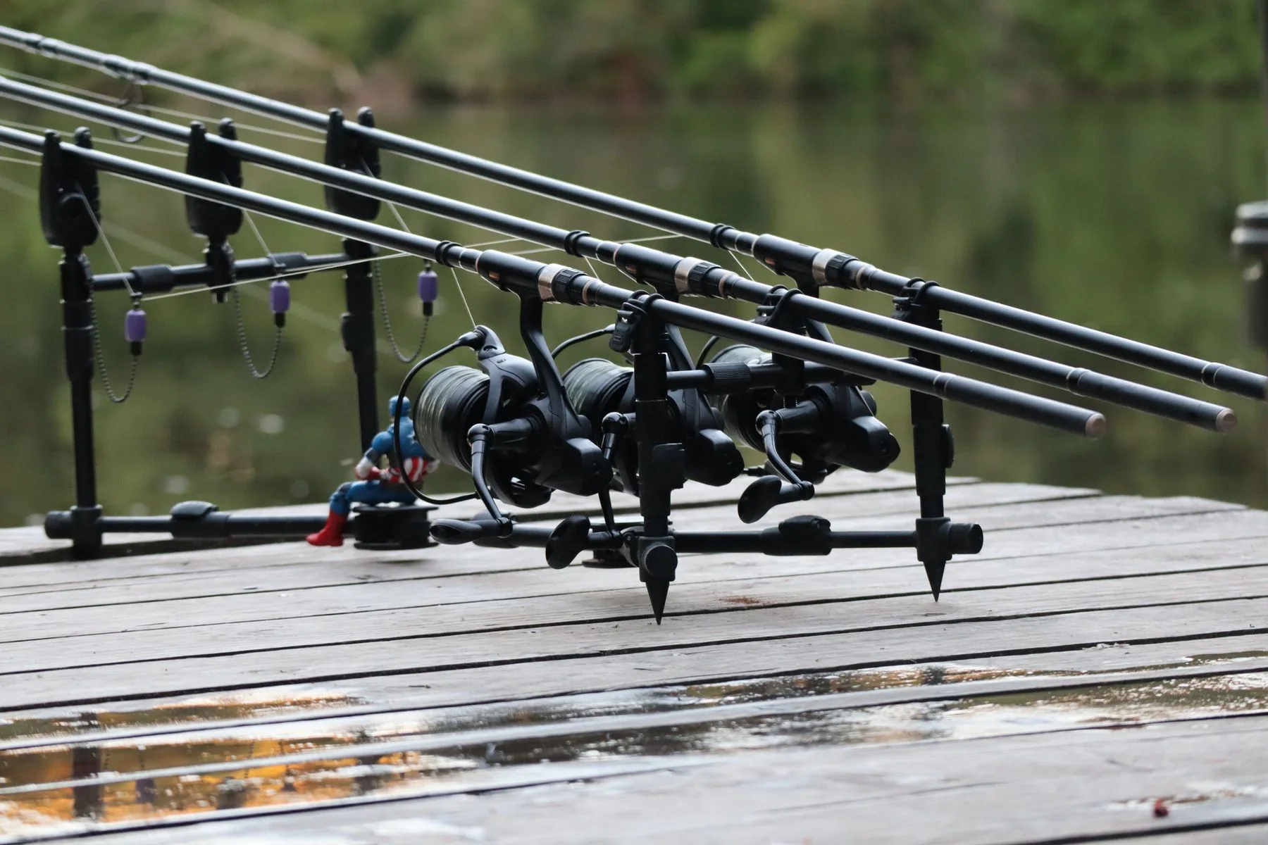 Fishing rods arranged on a wooden platform beside calm water.