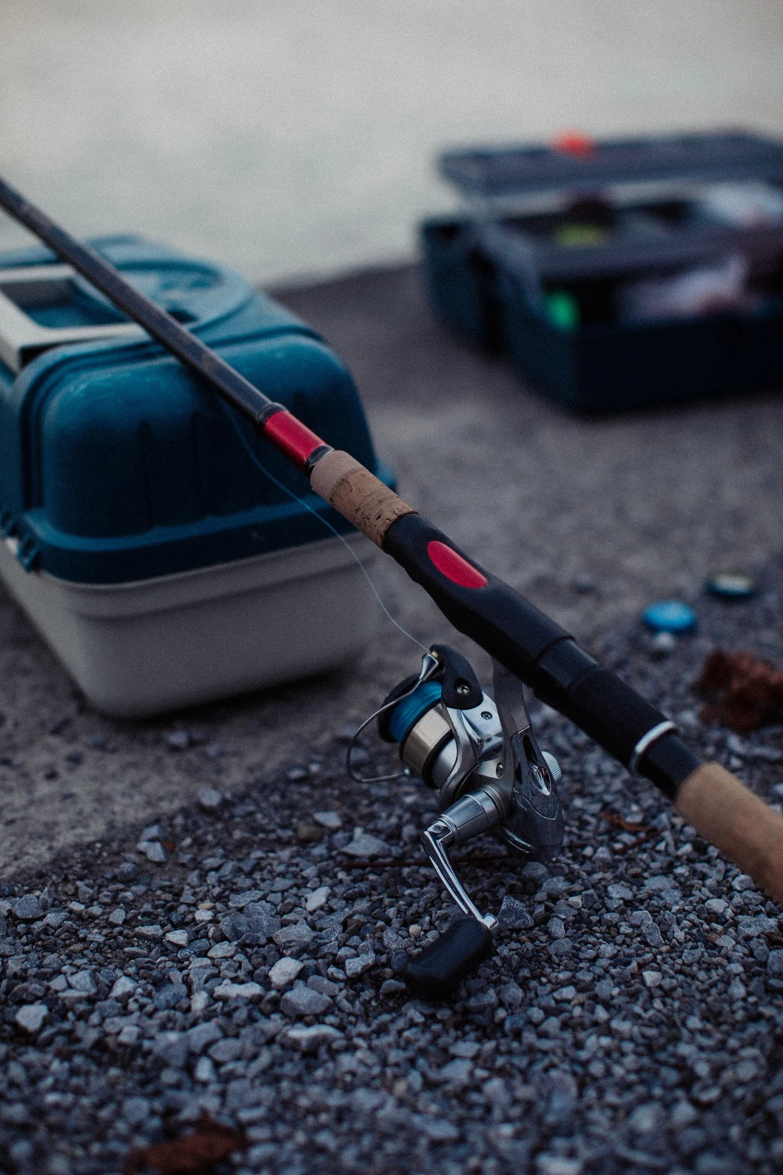 Fishing rod and tackle box resting on a gravel surface.