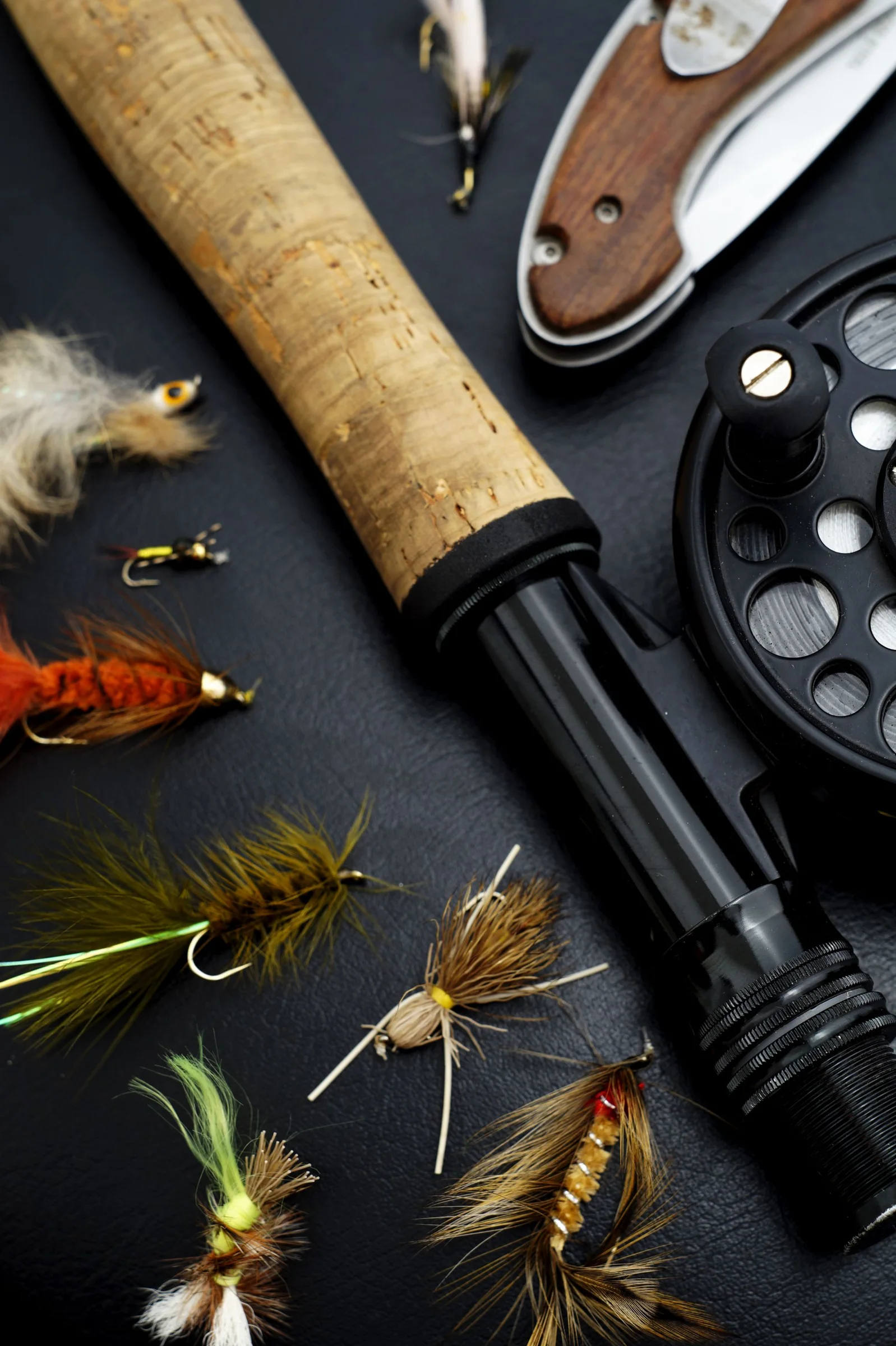 Fly fishing rod, reel and flies arranged on a dark surface.